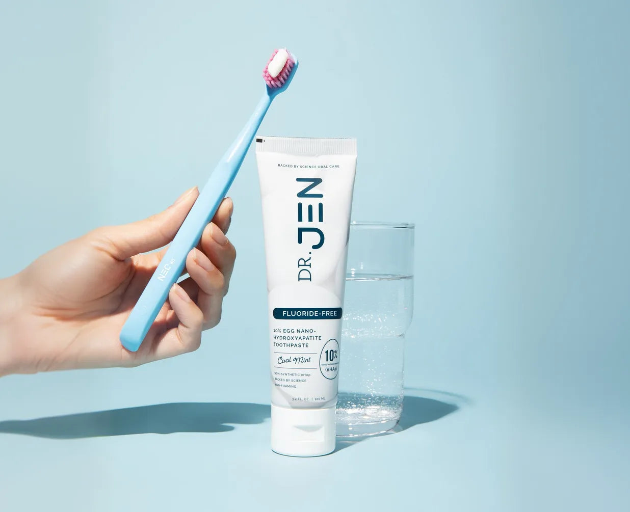 Hand holding a toothbrush next to a tube of Dr. Jen's Eggshell toothpaste