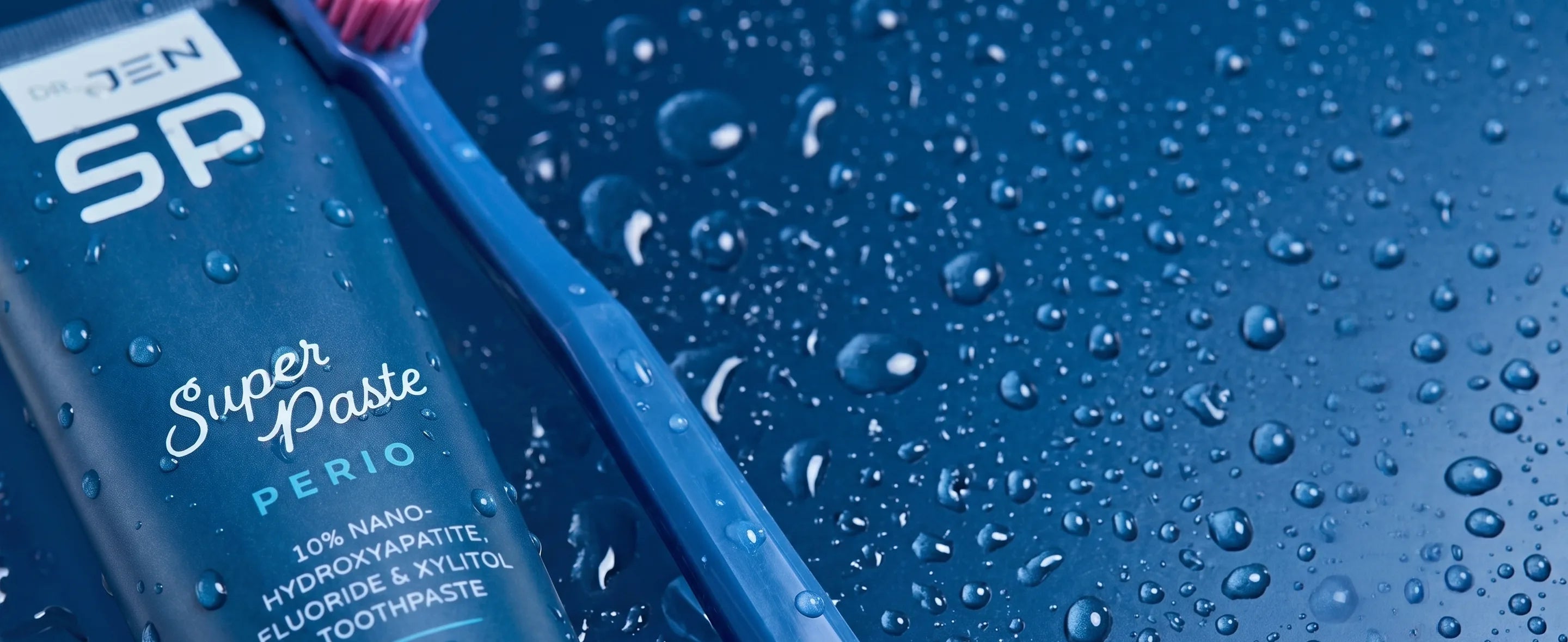 Dr. Jen's Super Paste Perio tube and toothbrush on a wet blue surface