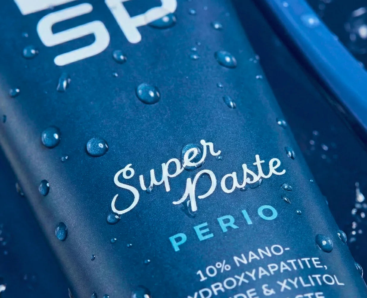 Dr. Jen's Super Paste Perio tube and toothbrush on a wet blue surface